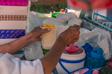 Artisanal shaved ice vendor prepares a portion, adding pineapple and other artisanal tropical...