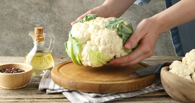 Woman putting whole cauliflower on wooden table, closeup