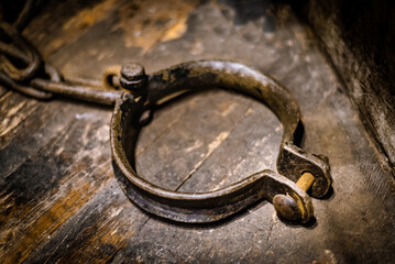 Ancient medieval wrought iron prisoner restraint, possibly fetter or leg cuff, on wooden floor.