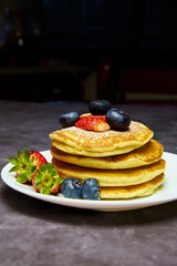 A plate of delicious pancakes in a tower with powdered sugar, decorated with blueberries and fresh berries (strawberries) for a wonderful breakfast.