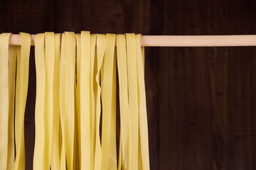 Fresh egg fettuccine noodles, drying in the foreground with a handmade wooden background with copy...