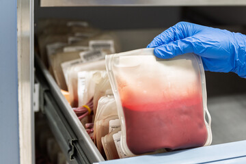 Close up scientist hand wear blue gloves holding red blood bag in storage refrigerator at blood...