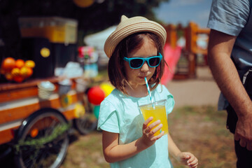 Little Girl Drinks Lemonade at a Kids Festival . Happy child enjoying summer vacation wearing...