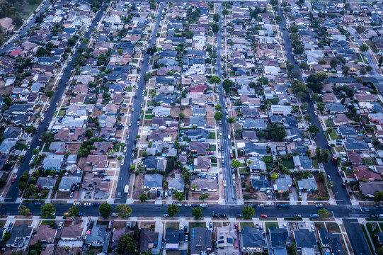 Aerial view of dense residential housing in Los Angeles, California, captured at dusk with visible street grids, cars, and urban sprawl under blue twilight tones