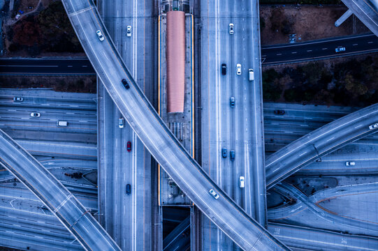 Aerial view of layered freeway overpasses in Los Angeles at twilight, with minimal traffic and graphic concrete lines forming a futuristic urban pattern
