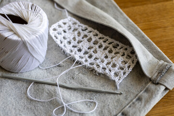 Process of creatively repair jeans shorts with crocheting patch and crochet hook and white cotton...