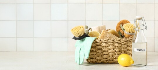 Basket with natural cleaning supplies, vinegar and lemons on light background with space for text