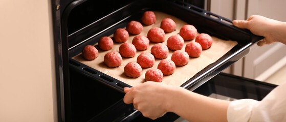 Woman putting baking tray with raw cutlets made of fresh forcemeat in oven, closeup