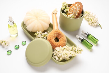 Bottles of cosmetic oil with loofah, brush and lilac twigs on white background