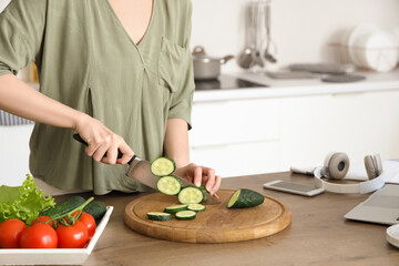 Woman cutting cucumber for salad on wooden table with vegetables