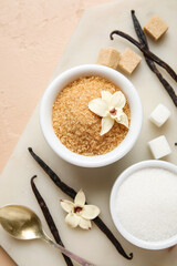 Bowls with aromatic vanilla sugar, flowers and sticks on beige background