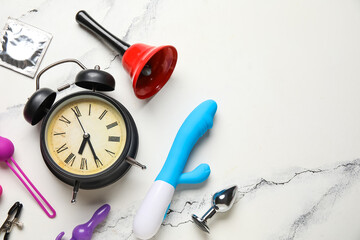 Alarm clock with different toys and condom on grunge white background. Time for sex