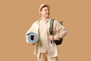 Fototapeta premium Young man with backpack and sleeping mat on brown background. Travel concept