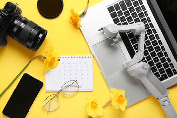 Calendar with stabilizer, photo camera, gadgets and daffodils on yellow background