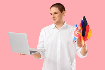 Young man with modern laptop and flags of different countries on pink background