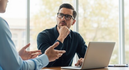 Photo of businessman in a meeting using a laptop and gesturing with his hands