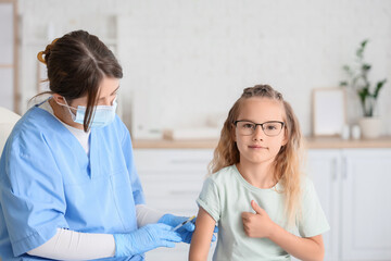 Fototapeta premium Little girl showing thumb-up while receiving vaccine from doctor in clinic