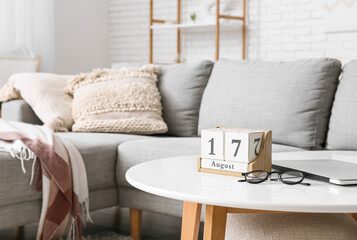 Cube calendar with date 17 AUGUST, eyeglasses and laptop on table in living room, closeup