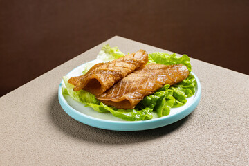Grilled Korean pork skin (Dwaeji-kkeopdegi) on a hot plate, served sizzling with dipping sauce. A chewy and savory street food often enjoyed as a Korean barbecue side dish or drinking snack.