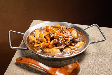 Side view of Korean black bean paste tteokbokki (Jjajang-tteokbokki) with glossy sauce. A savory and chewy Korean rice cake dish covered in sweet black bean glaze, served as a fusion comfort food.
