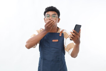 Young shocked asian man barista bartender barman employee in blue apron work in coffee shop using mobile cell phone cover mouth with hands isolated on white background Small business startup
