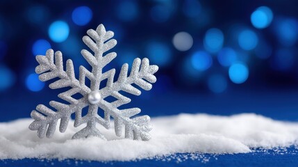 Close-up of a single snowflake resting on white snow with a smooth blue background, winter detail.