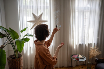 Calm woman lighting palo santo stick, filling home with fragrant smoke for improved wellbeing....