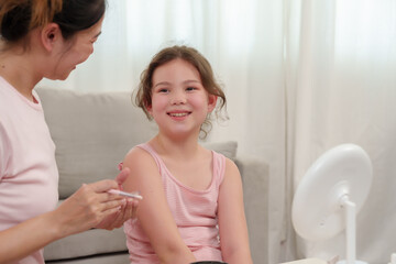 Asian single mother smiling at young daughter during happy beauty session at home, girl sitting...