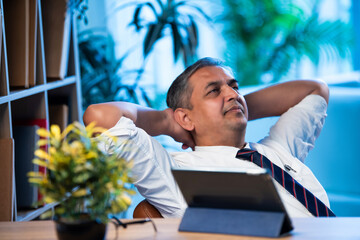 Asian executive leans back on chair at office desk, taking a break from work