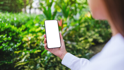 Mockup image of a woman holding mobile phone with blank white desktop screen in the nature outdoors