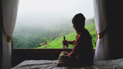 A woman playing with a cat while sitting on bed with a beautiful nature view on foggy morning