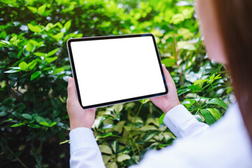 Mockup image of a woman holding digital tablet with blank white desktop screen in the nature...