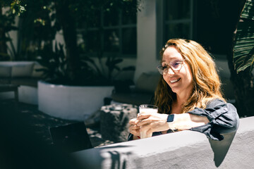 Relaxed Woman with Red Hair Drinking Milk Outdoors in Sunny Garden Office Setting