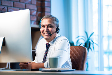Indian call center agent wearing headset and working on computer in corporate office
