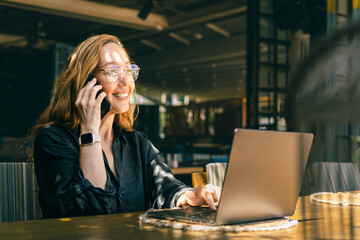 Happy woman working remotely with laptop and smartphone at cafe, enjoying flexible work lifestyle
