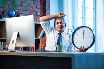 Frustrated Indian employee holds wall clock in office, symbolizing overtime and imbalance