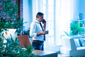 Indian executive multitasks with coffee and phone call inside contemporary office setting