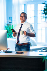 Indian executive multitasks with coffee and phone call inside contemporary office setting