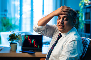 Indian investor appears stressed after stock market crash, laptop shows falling graph