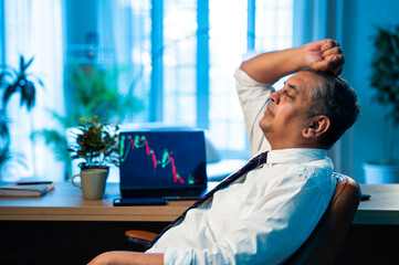 Indian investor appears stressed after stock market crash, laptop shows falling graph