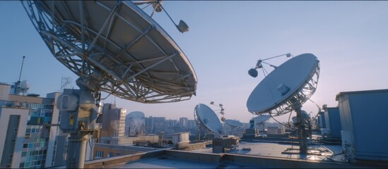 A view of several satellite dishes on a rooftop with a city skyline in the background during daytime