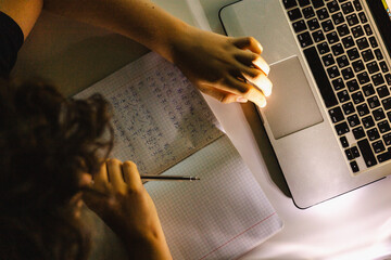 Teen learning Japanese language, writing in notebook while using laptop, top-down evening shot