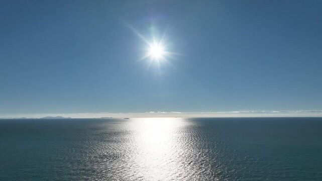 Drone tilt-down shot capturing the sun reflecting off the ocean surface under a blue sky