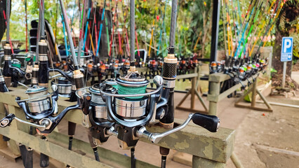 A row of fishing rods with spinning reels neatly arranged on a wooden rack. The image showcases...