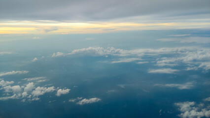 This image shows a beautiful view from above the clouds, taken from an airplane window. Fluffy cumulus clouds rise slowly over the vast landscape below.