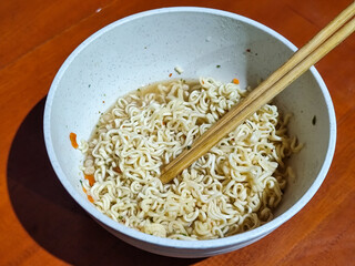 Chewy white instant noodles are held up in a white bowl, highlighting their texture and...