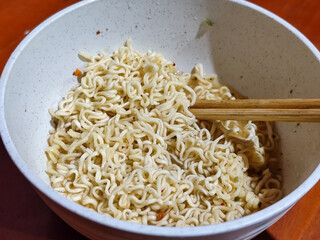 Chewy white instant noodles are held up in a white bowl, highlighting their texture and...