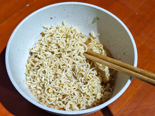 Chewy white instant noodles are held up in a white bowl, highlighting their texture and deliciousness, against the blurry background of the bowl.