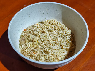 Chewy white instant noodles are held up in a white bowl, highlighting their texture and...