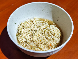 Chewy white instant noodles are held up in a white bowl, highlighting their texture and...